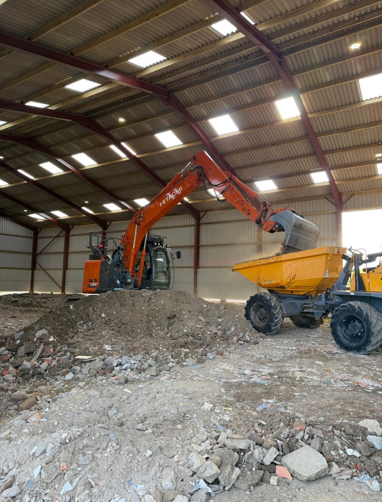 Hitachi excavator loading a site dumper inside an industrial building